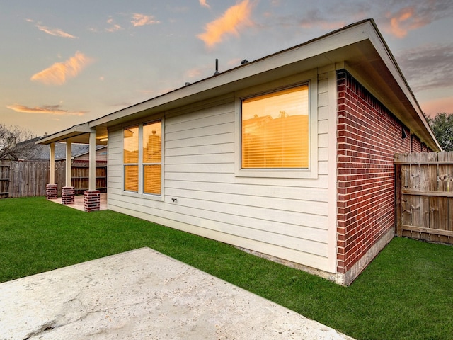 property exterior at dusk featuring a patio area and a lawn