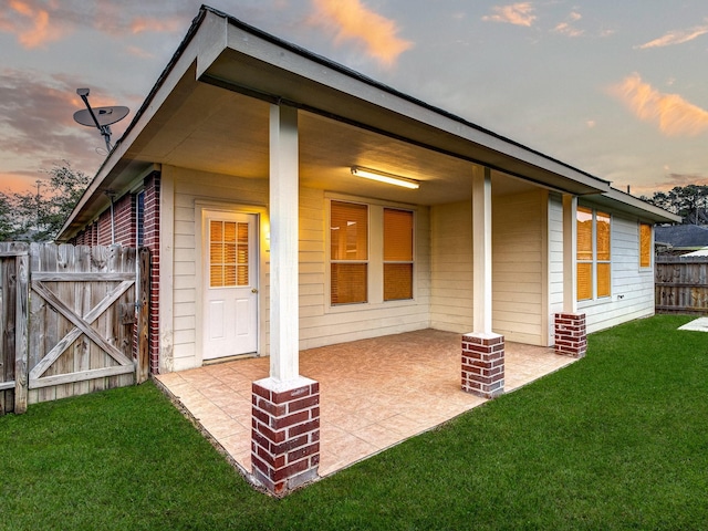 back house at dusk featuring a patio area and a yard