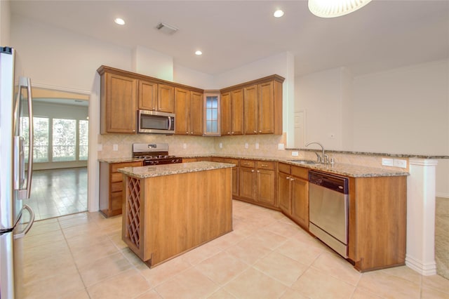 kitchen with kitchen peninsula, sink, appliances with stainless steel finishes, light tile patterned floors, and light stone counters