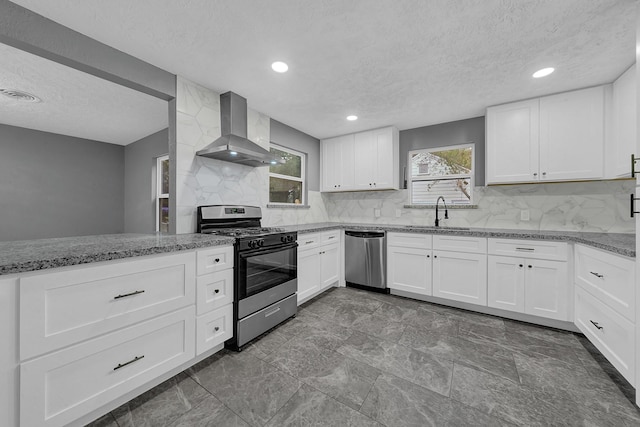 kitchen with white cabinetry, stainless steel dishwasher, wall chimney exhaust hood, and range with gas stovetop