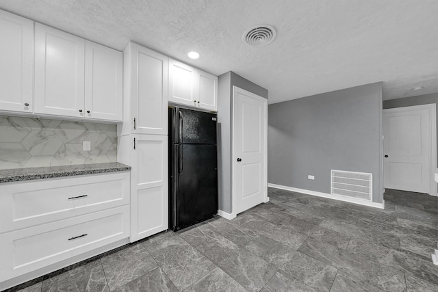 kitchen featuring white cabinetry, black refrigerator, backsplash, stone countertops, and a textured ceiling