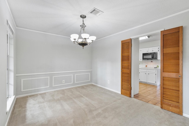 empty room with light carpet, a textured ceiling, a chandelier, and crown molding