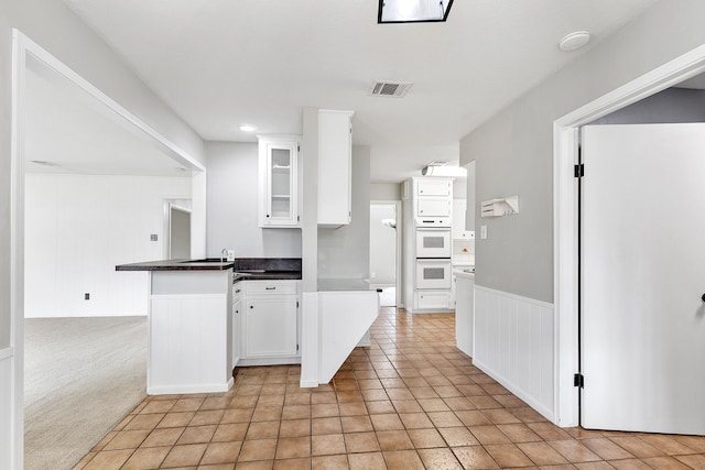 kitchen with light colored carpet, white double oven, kitchen peninsula, wooden walls, and white cabinetry