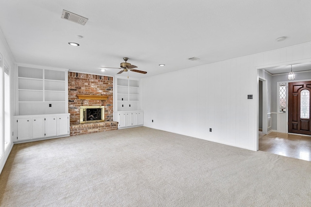 unfurnished living room with light carpet, ceiling fan, built in features, a brick fireplace, and crown molding