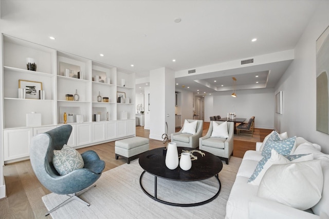 living area featuring light wood-style floors, a tray ceiling, visible vents, and recessed lighting