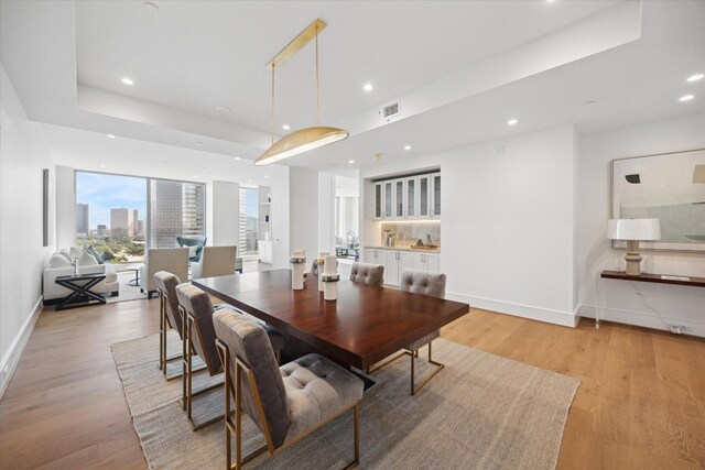 dining room featuring a view of city, recessed lighting, a raised ceiling, light wood-type flooring, and baseboards