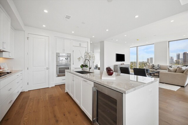 kitchen featuring an island with sink, beverage cooler, open floor plan, and a sink