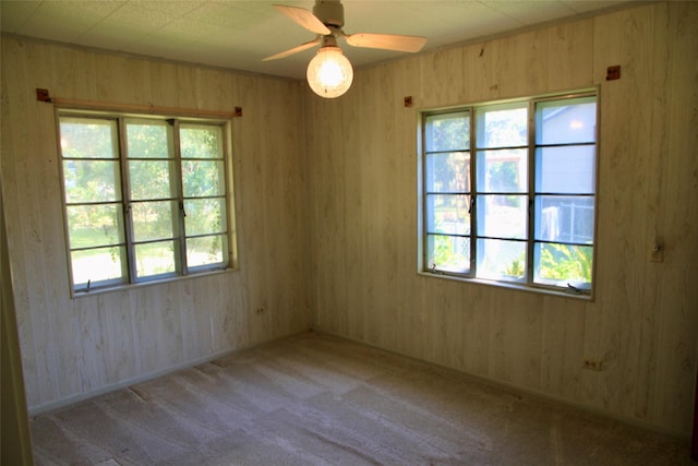 empty room featuring ceiling fan, light colored carpet, and wooden walls