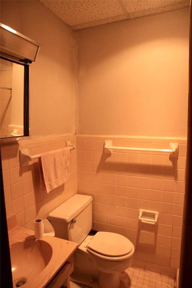 bathroom featuring toilet, tile walls, tile patterned flooring, sink, and a paneled ceiling