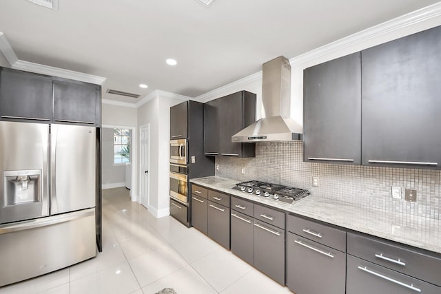 kitchen featuring backsplash, light stone countertops, appliances with stainless steel finishes, ornamental molding, and wall chimney exhaust hood