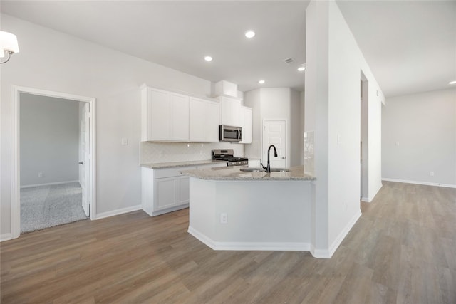 kitchen with tasteful backsplash, light hardwood / wood-style floors, white cabinetry, light stone countertops, and appliances with stainless steel finishes