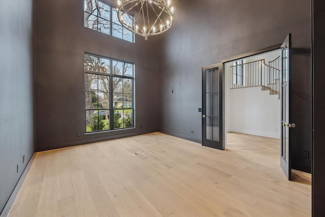 unfurnished room featuring a towering ceiling, a chandelier, and light wood-type flooring