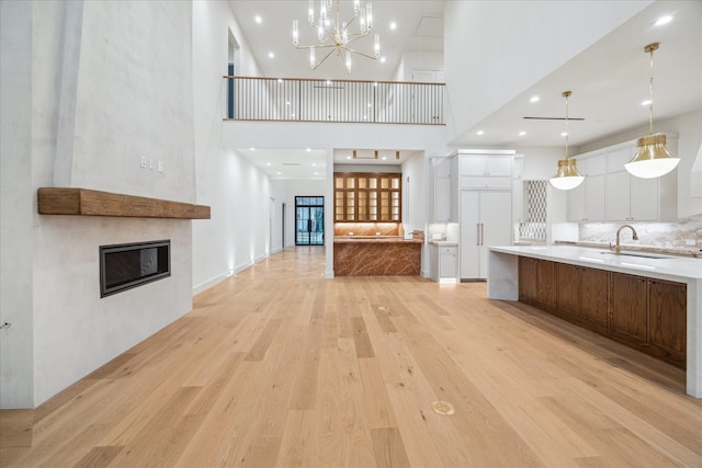 unfurnished living room featuring sink, a towering ceiling, and light wood-type flooring