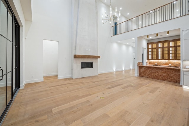 unfurnished living room featuring a towering ceiling, an inviting chandelier, a fireplace, and light hardwood / wood-style flooring