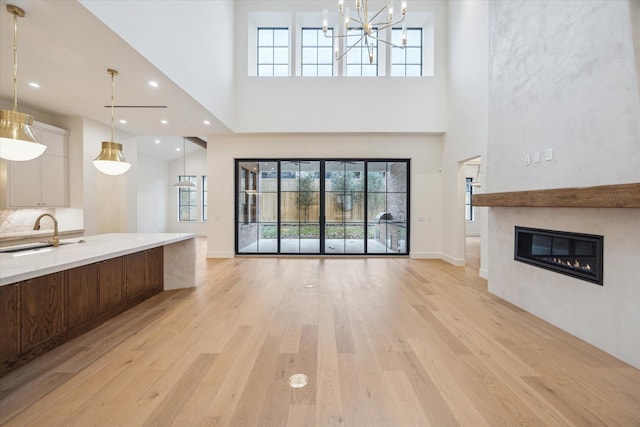 unfurnished living room featuring light wood-type flooring, a wealth of natural light, sink, and a high ceiling