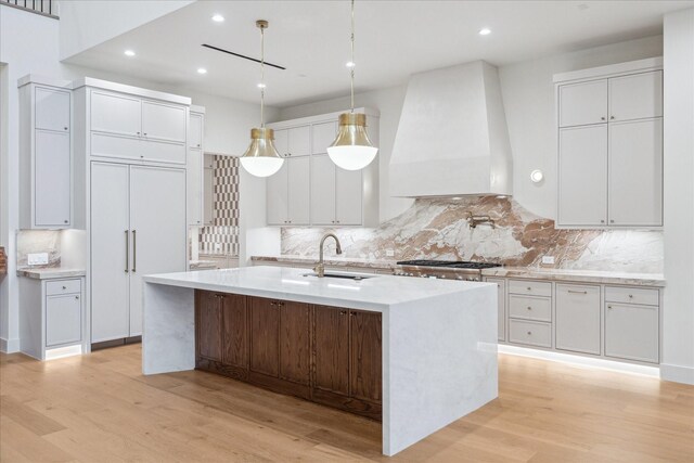 kitchen with white cabinetry, premium range hood, sink, and a kitchen island with sink