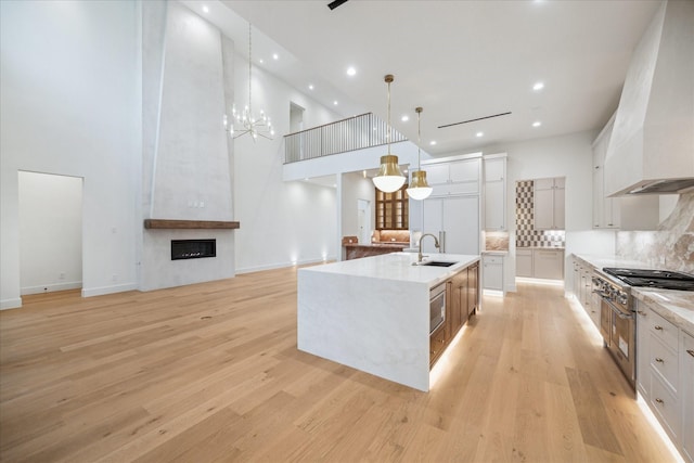 kitchen with decorative light fixtures, an island with sink, white cabinets, backsplash, and custom range hood