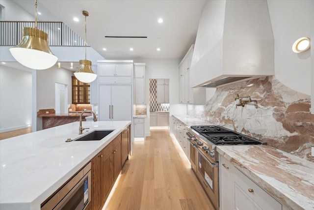 kitchen featuring sink, white cabinetry, light stone counters, custom range hood, and pendant lighting