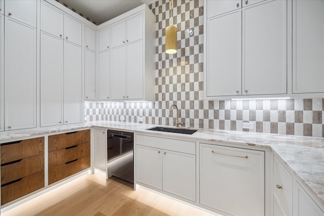 kitchen featuring light stone counters, black dishwasher, sink, and white cabinets