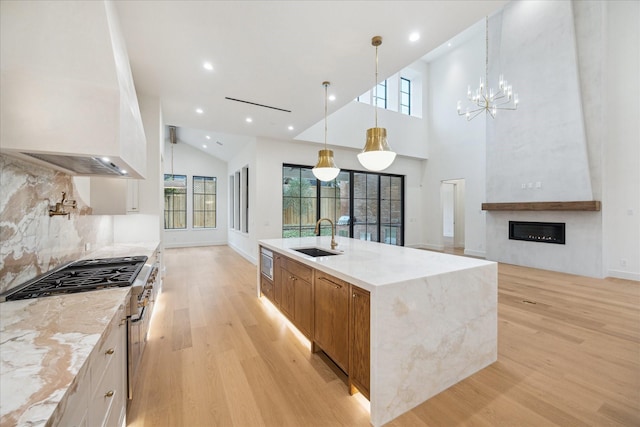 kitchen with a spacious island, sink, light stone counters, hanging light fixtures, and appliances with stainless steel finishes