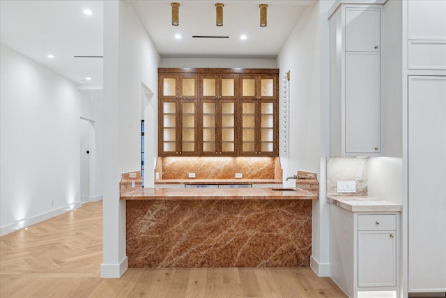 interior space with white cabinetry, backsplash, sink, and light parquet flooring