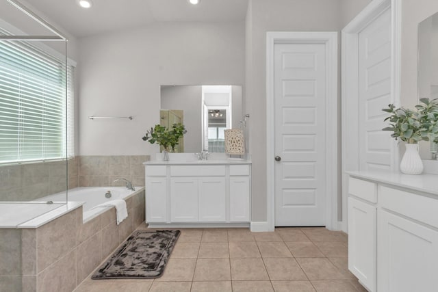 bathroom featuring a wealth of natural light, tile patterned floors, vanity, and a relaxing tiled tub