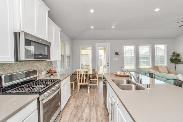 kitchen with lofted ceiling, white cabinetry, stainless steel appliances, decorative backsplash, and sink