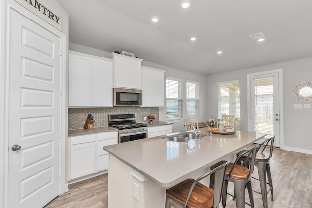 kitchen with stainless steel appliances, white cabinetry, a breakfast bar, and an island with sink