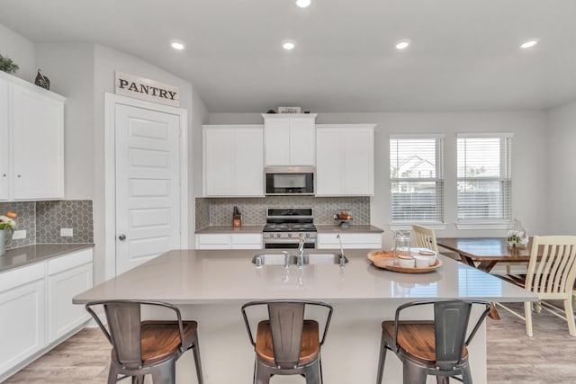 kitchen with appliances with stainless steel finishes, white cabinetry, sink, a kitchen breakfast bar, and a kitchen island with sink