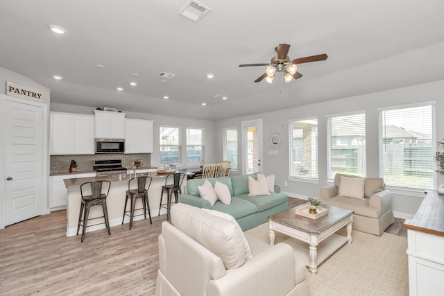 living room with ceiling fan, light hardwood / wood-style flooring, and vaulted ceiling