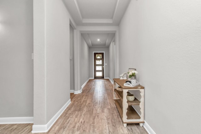 doorway to outside with a raised ceiling and light wood-type flooring