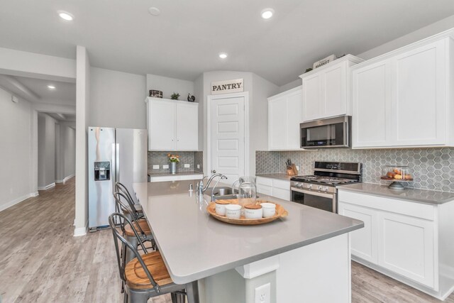 kitchen featuring a breakfast bar area, stainless steel appliances, white cabinetry, and a center island with sink