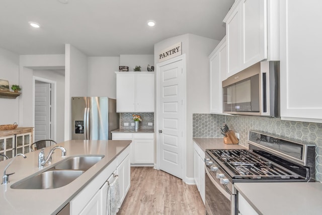 kitchen featuring appliances with stainless steel finishes, white cabinetry, tasteful backsplash, light hardwood / wood-style floors, and sink