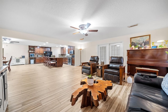 living room featuring light wood-type flooring, french doors, a textured ceiling, and ceiling fan