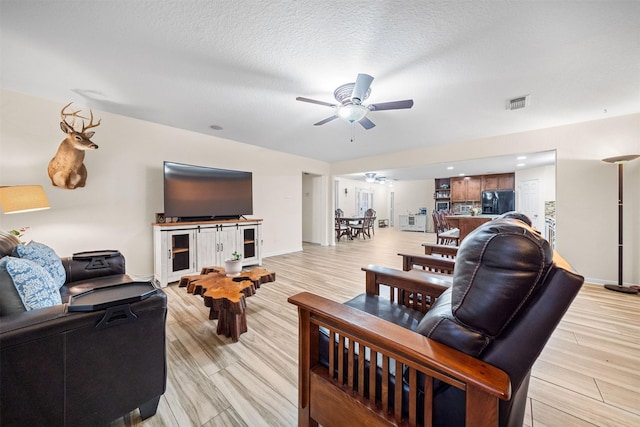 living room with a textured ceiling, ceiling fan, and light hardwood / wood-style flooring