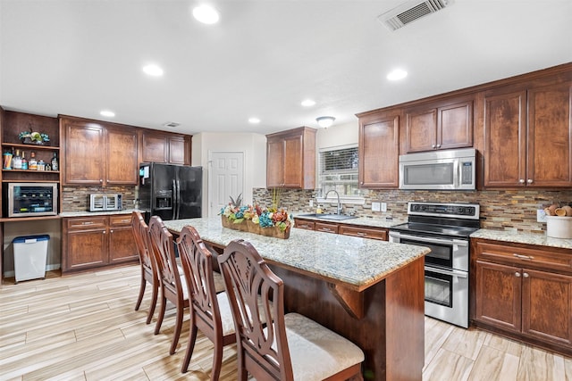 kitchen featuring a center island, a kitchen bar, sink, appliances with stainless steel finishes, and light stone counters