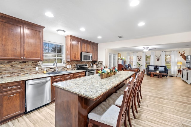 kitchen featuring ceiling fan, appliances with stainless steel finishes, sink, light stone countertops, and a center island