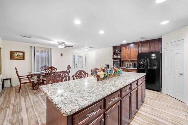 kitchen featuring a kitchen island, black refrigerator with ice dispenser, light hardwood / wood-style floors, ceiling fan, and light stone counters