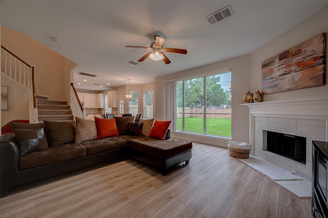 living room featuring ceiling fan with notable chandelier, light hardwood / wood-style floors, and a fireplace