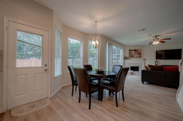 dining room with ceiling fan with notable chandelier, a textured ceiling, and light wood-type flooring