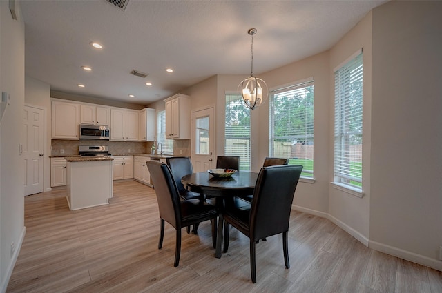 dining area featuring sink, a healthy amount of sunlight, a chandelier, and light wood-type flooring