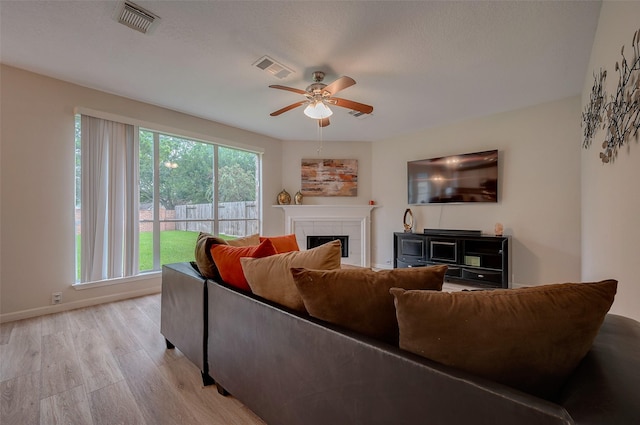 living room with ceiling fan, light wood-type flooring, and a tiled fireplace