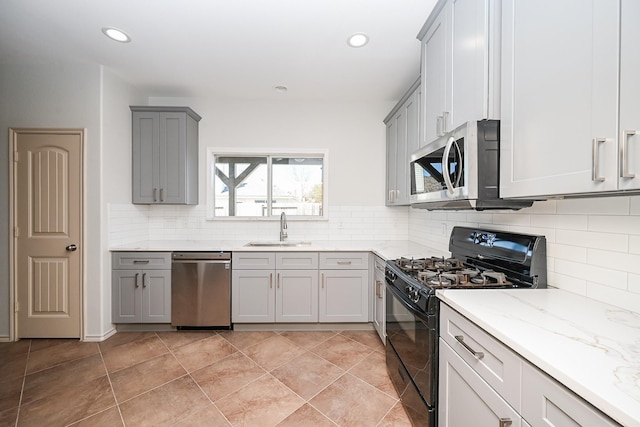 kitchen featuring appliances with stainless steel finishes, gray cabinetry, tasteful backsplash, light stone counters, and sink