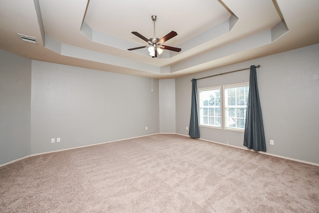 empty room with ceiling fan, light carpet, and a raised ceiling