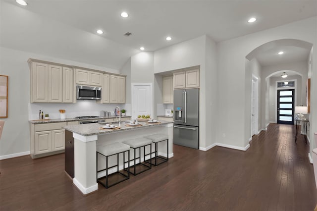 kitchen with sink, a breakfast bar area, stainless steel appliances, light stone counters, and an island with sink