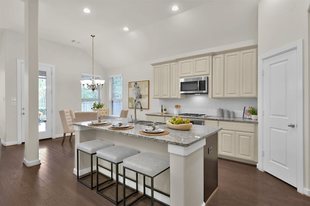 kitchen with vaulted ceiling, pendant lighting, a kitchen island with sink, stainless steel appliances, and cream cabinetry