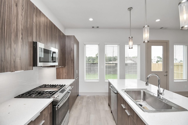 kitchen featuring appliances with stainless steel finishes, decorative light fixtures, decorative backsplash, sink, and light wood-type flooring