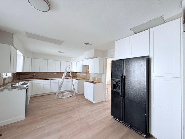 kitchen featuring black fridge, a textured ceiling, light hardwood / wood-style floors, and white cabinets