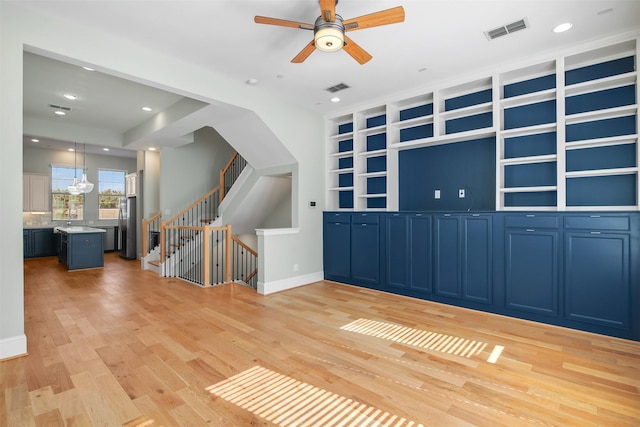 unfurnished living room featuring ceiling fan, built in shelves, and light wood-type flooring