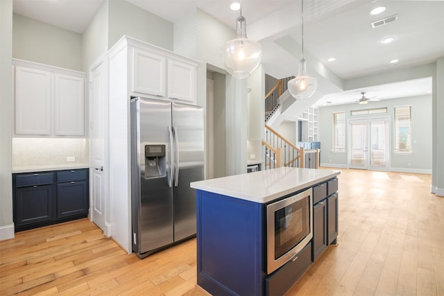 kitchen featuring appliances with stainless steel finishes, pendant lighting, blue cabinets, and white cabinets